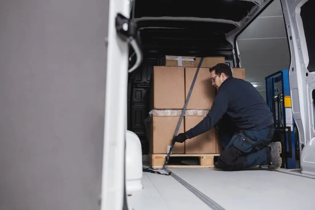 Man secures a pallet full of boxes in his cargo van. View from the van trunk.
